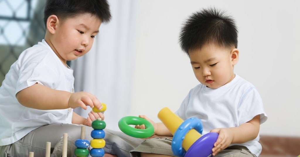 Two young boys playing with colorful stacking toys on a soft surface, focused and engaged in their activity.