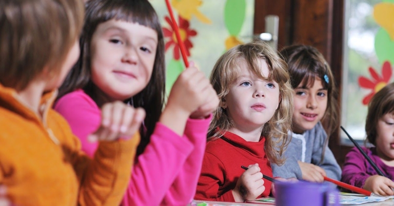 A group of children engaged in an art activity, smiling and focused, with colorful decorations in the background.