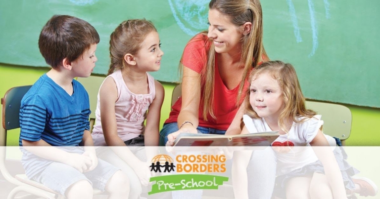 A cheerful teacher engages three children in a reading activity, fostering a love for books and learning together.