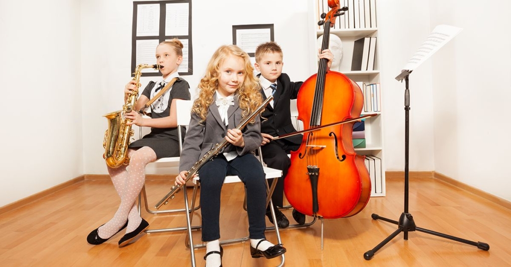 young musicians: a girl with a flute, a boy with a saxophone, and another boy with a cello, all dressed in formal attire.