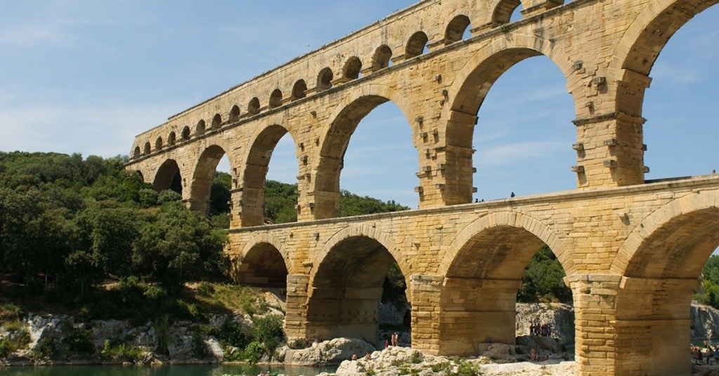 The ancient Pont du Gard aqueduct, showcasing its impressive stone arches against a clear blue sky and lush greenery.