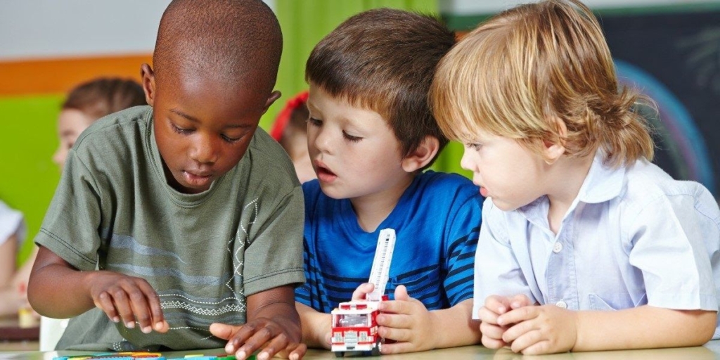 Three young boys collaborate on a project at a table, showcasing teamwork and engagement in a classroom setting.