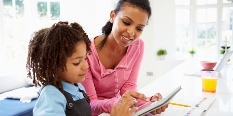 A mother and daughter share a moment, with the mother guiding her on a tablet, promoting interactive learning at home.