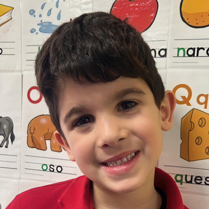 A happy boy with dark hair smiles brightly against a colorful educational backdrop, showcasing his cheerful personality.