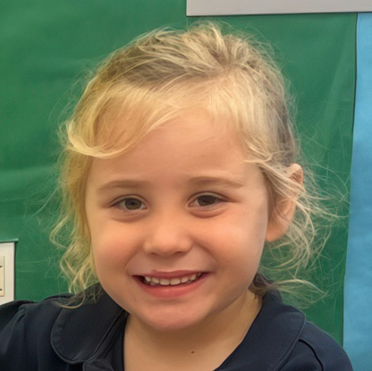 A smiling girl with curly blonde hair poses for the camera, exuding joy and a playful spirit against a green background.