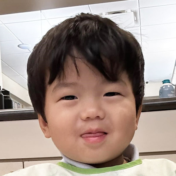 A cute boy with dark hair smiles brightly at the camera, showcasing a playful expression and a hint of his tongue.