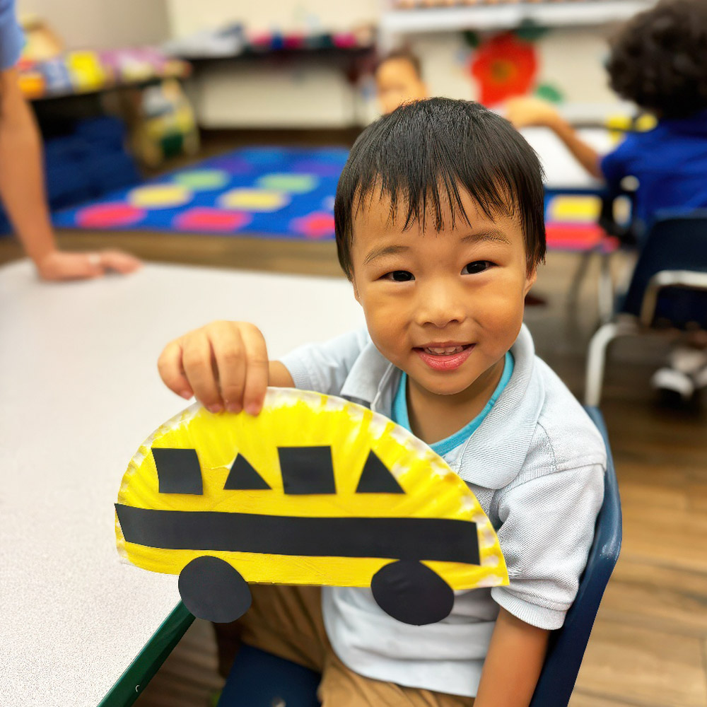 A cheerful child holds up a handmade yellow school bus craft, showcasing creativity and pride in their work.