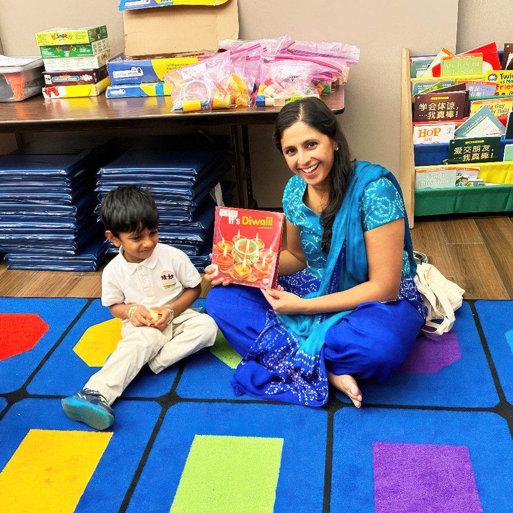 A parent in blue attire sits with a child, holding a book about Diwali, sharing joy and cultural traditions together.