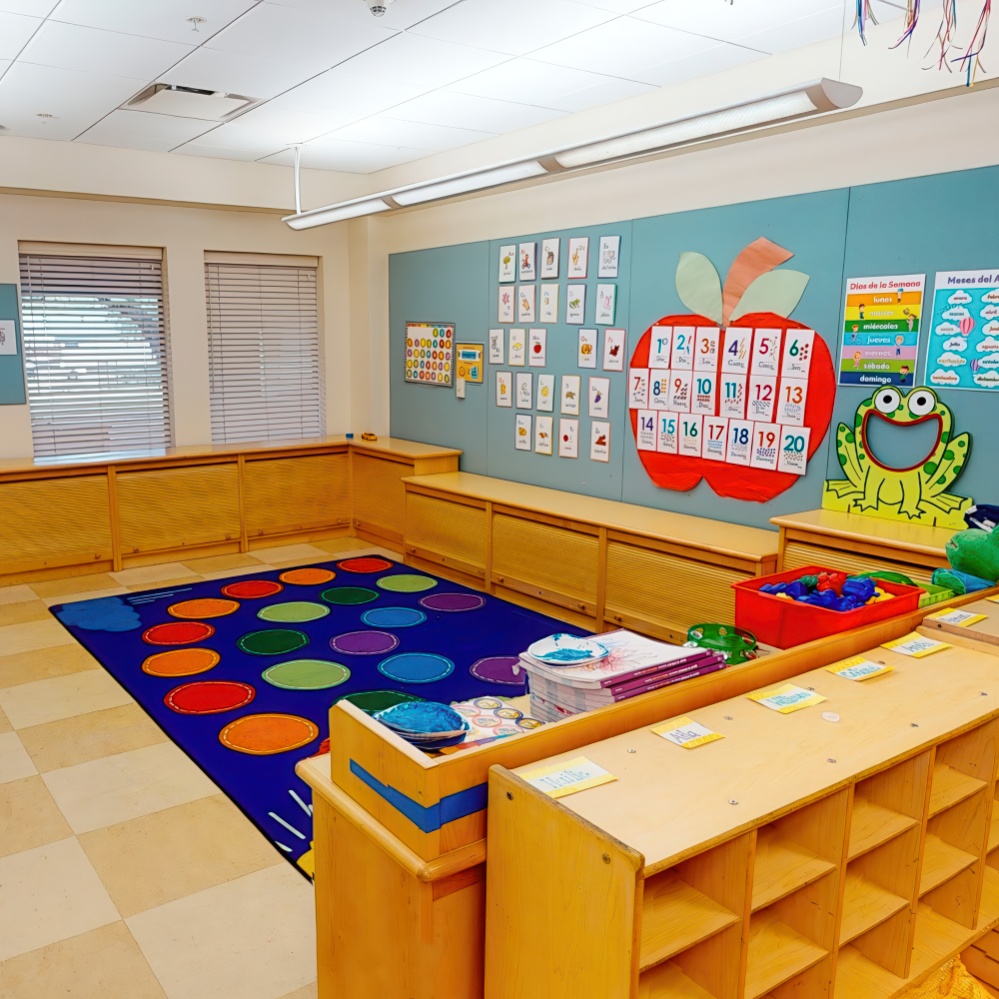 A bright classroom with a colorful rug, educational posters, and wooden seating, creating a welcoming learning space.