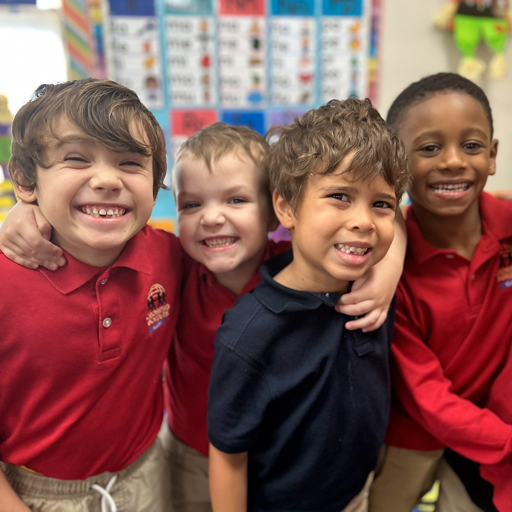 Four smiling boys pose closely together, showing their joy and friendship in a colorful classroom setting.