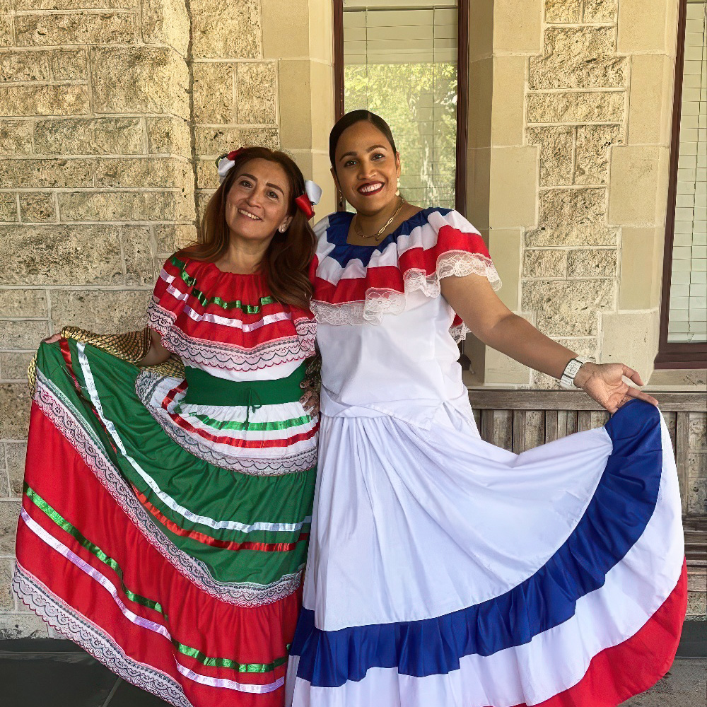 Two teacher in traditional dresses pose joyfully outdoors, celebrating cultural heritage with vibrant attire.