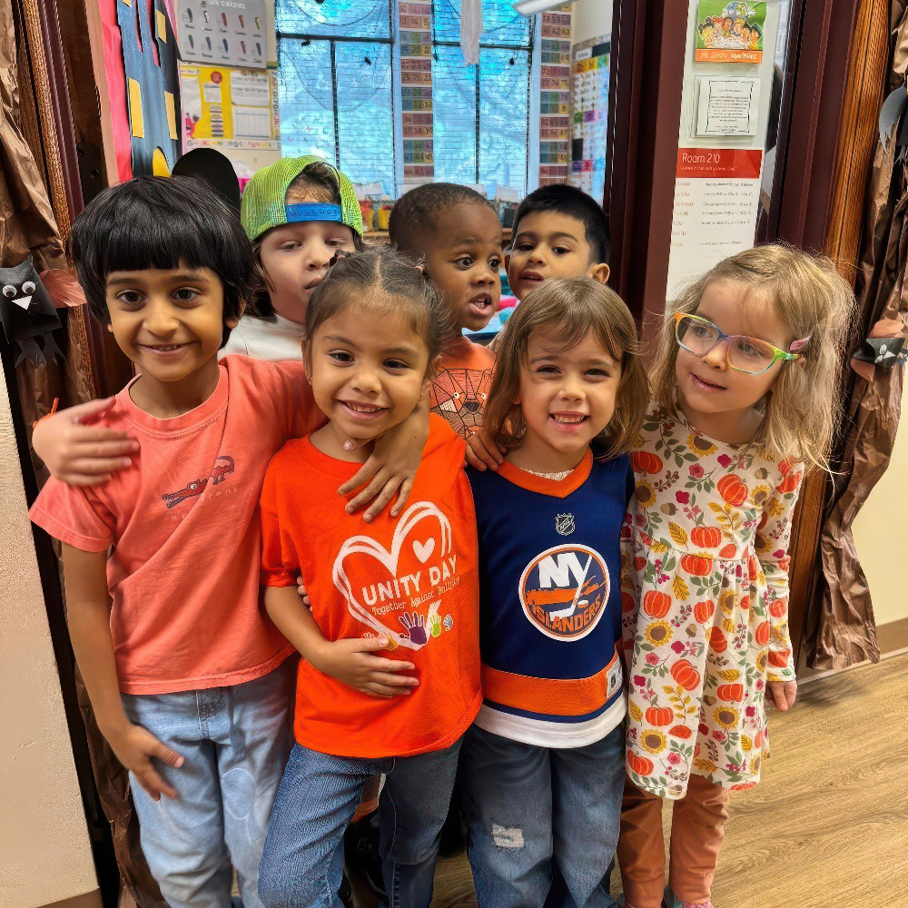 A cheerful group of six children poses together, smiling and wearing colorful outfits, showcasing their friendship and joy.