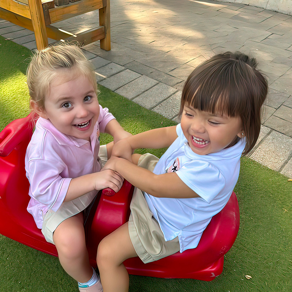 Two girls joyfully play together on a red ride, sharing laughter and friendship in an outdoor setting.