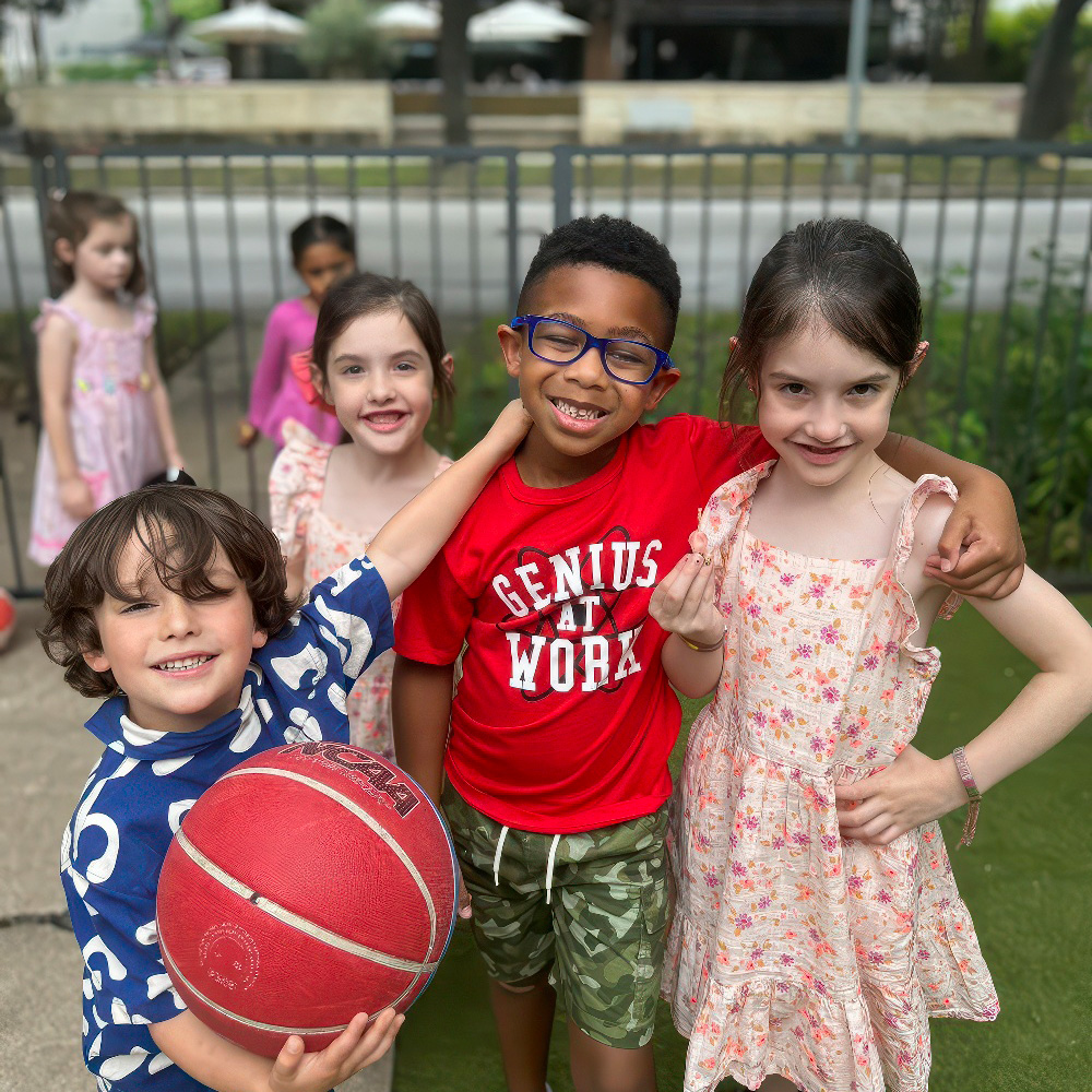 A group of smiling kids poses outdoors, one holding a basketball, capturing their friendship and enjoyment.