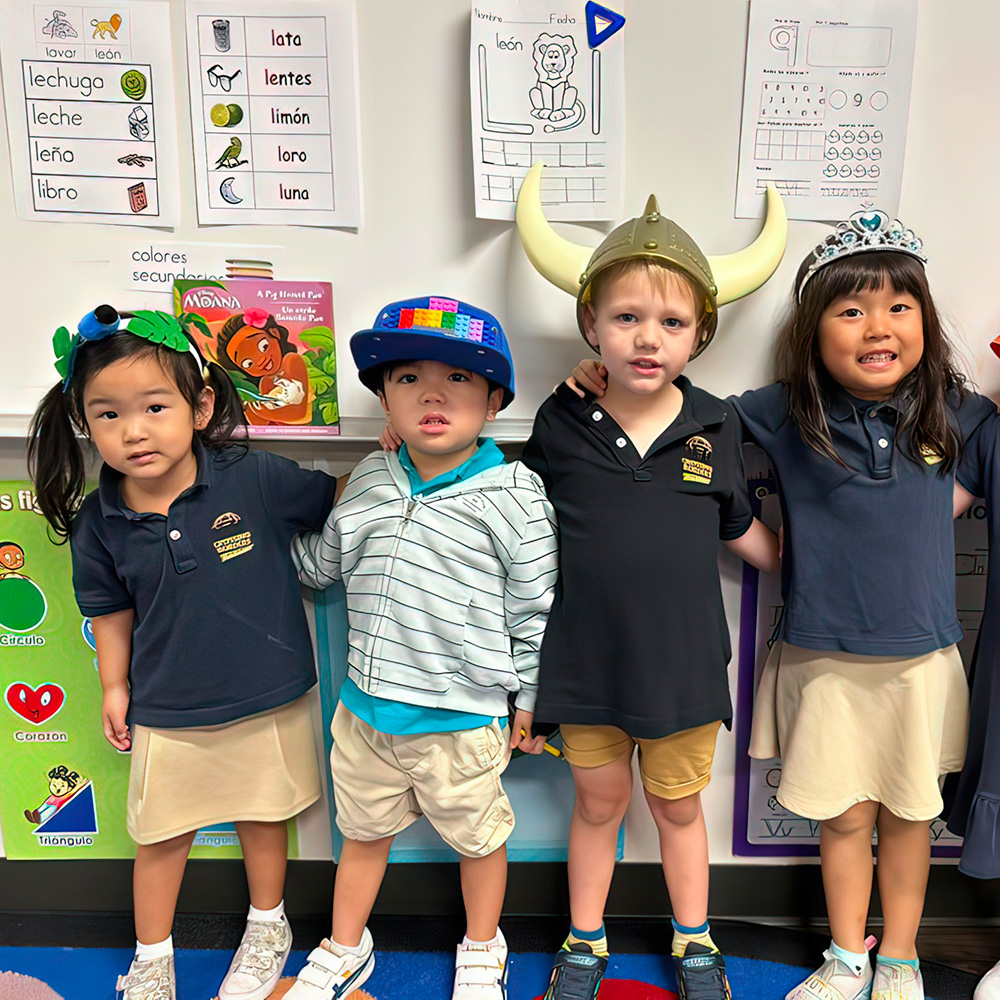 Four kids in matching shirts wear fun hats and pose together, showcasing their playful spirit in a classroom.