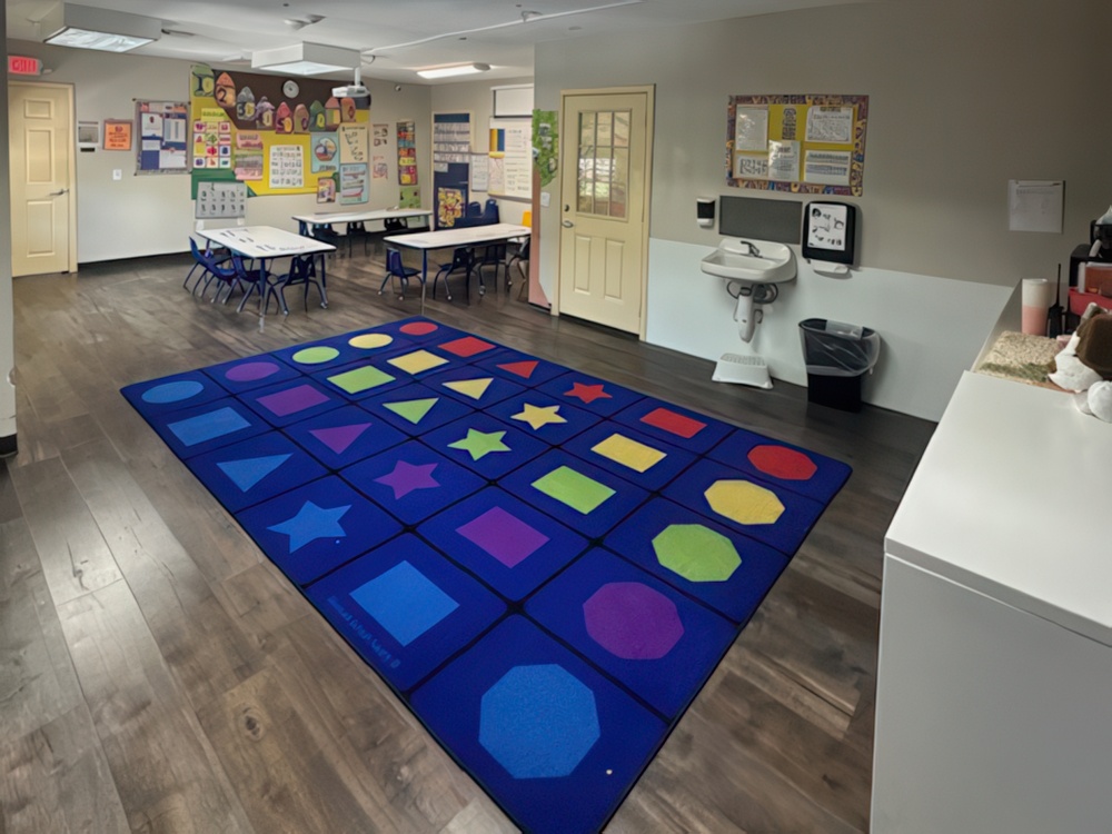 A bright classroom features small tables and chairs and walls adorned with classroom decorations designed for preschoolers.