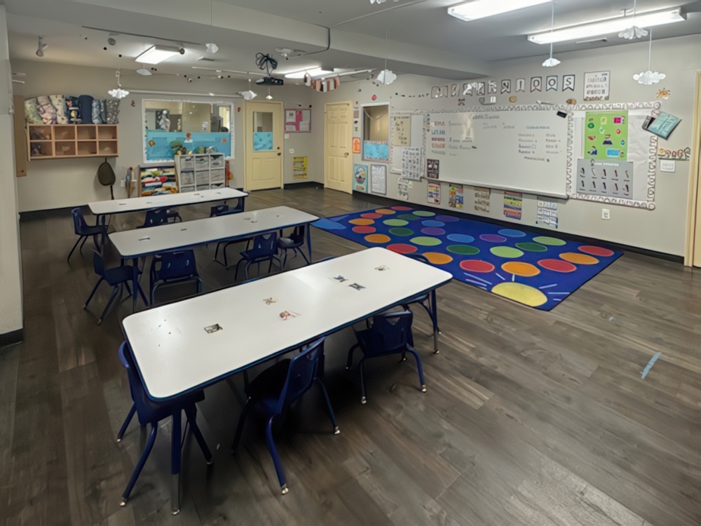 A bright classroom features small tables and chairs and walls adorned with classroom decorations designed for preschoolers.