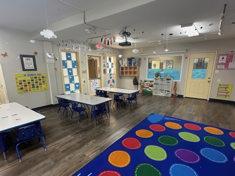 A bright classroom features small tables and chairs and walls adorned with classroom decorations designed for preschoolers.