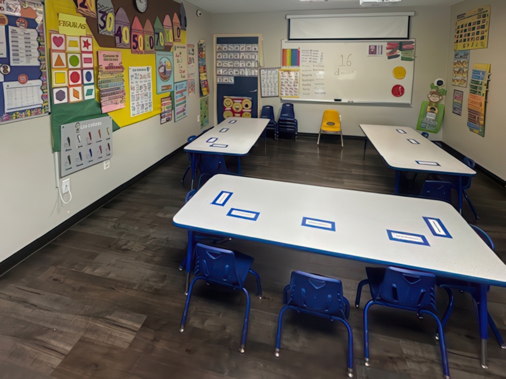 A bright classroom features small tables and chairs and walls adorned with classroom decorations designed for preschoolers.