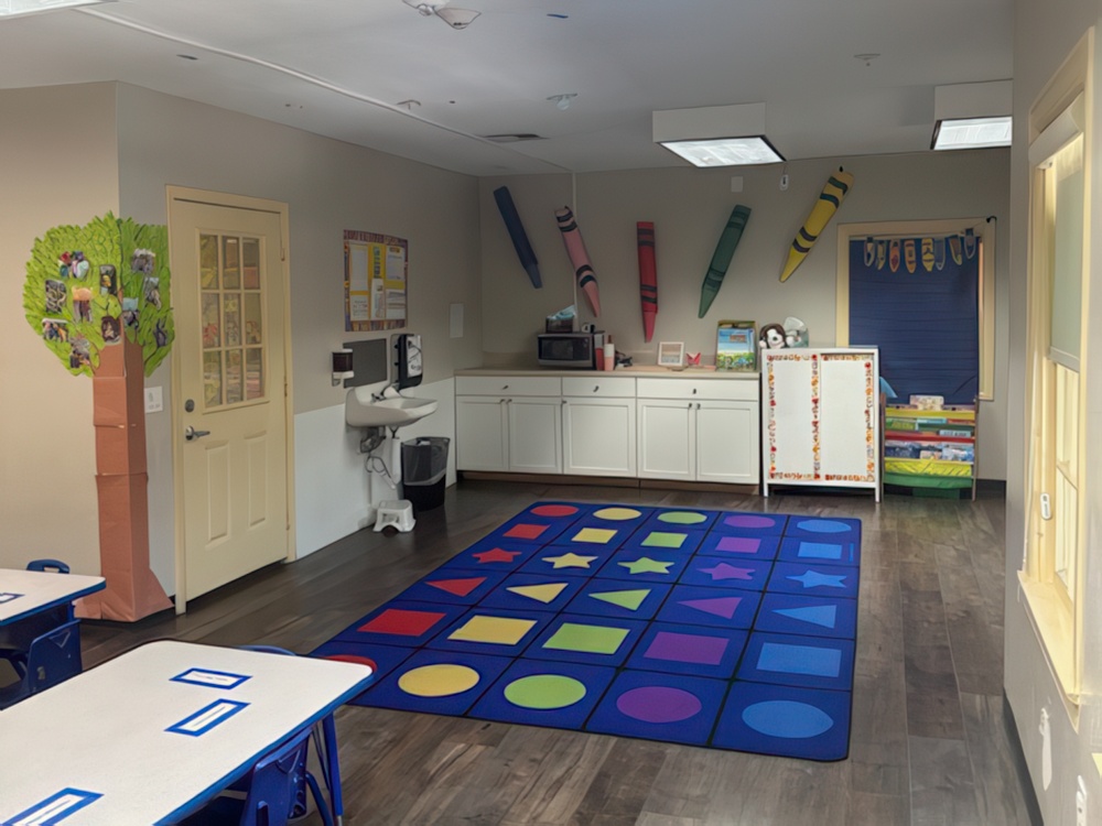 A bright classroom features small tables and chairs and walls adorned with classroom decorations designed for preschoolers.