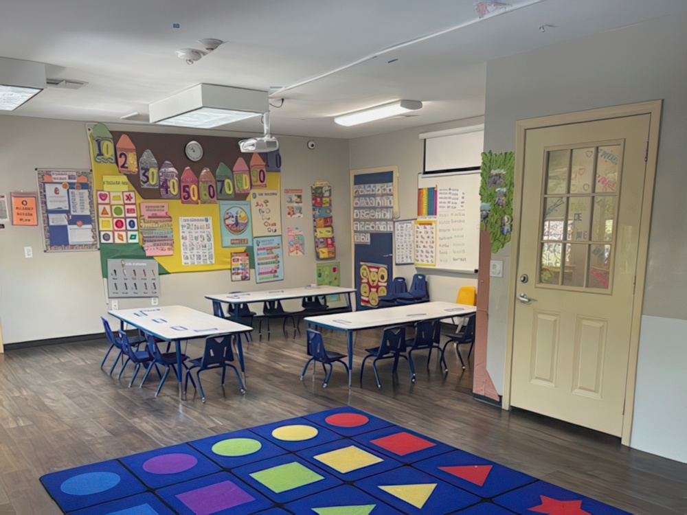 A bright classroom features small tables and chairs and walls adorned with classroom decorations designed for preschoolers.