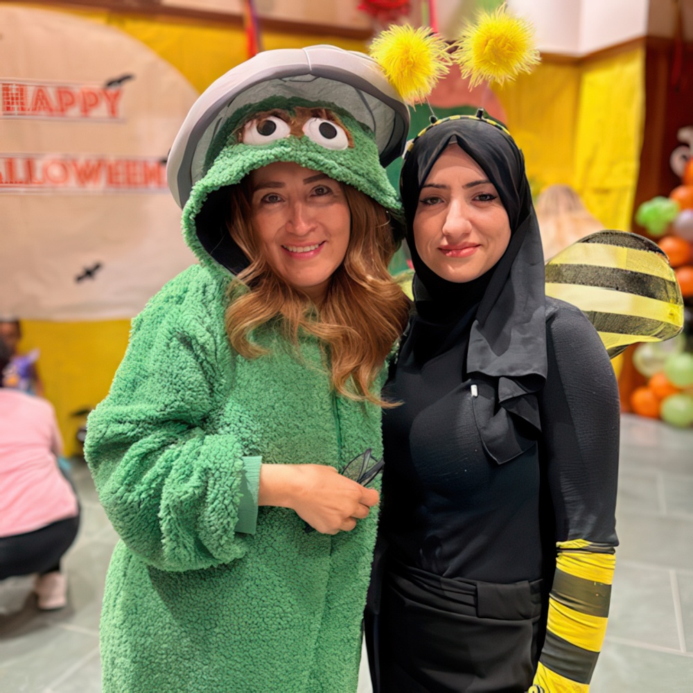 Two teacher, one in a green costume and the other in a bee outfit, pose together with smiles at a fun event.