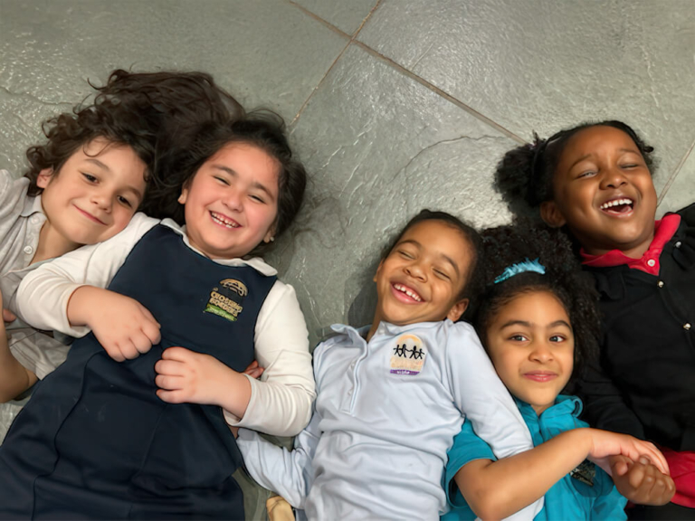 Five children lie on the floor, smiling and laughing together, enjoying each other's company in a playful moment.