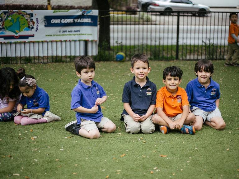 A group of children sits on grass, some playing and others posing, with a colorful banner in the background.