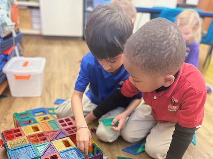 Two children collaborate on a colorful building project with geometric shapes in a playful classroom environment.