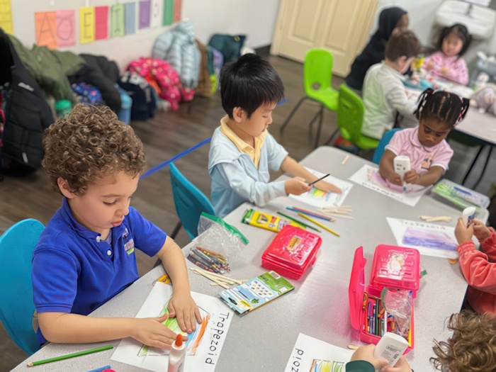 Children work on art projects at a table, using crayons and glue in a vibrant classroom setting.