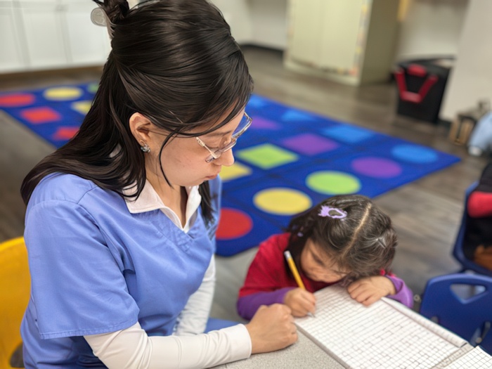 A teacher assists a young girl with her work at a table, fostering a supportive learning atmosphere in a vibrant classroom.