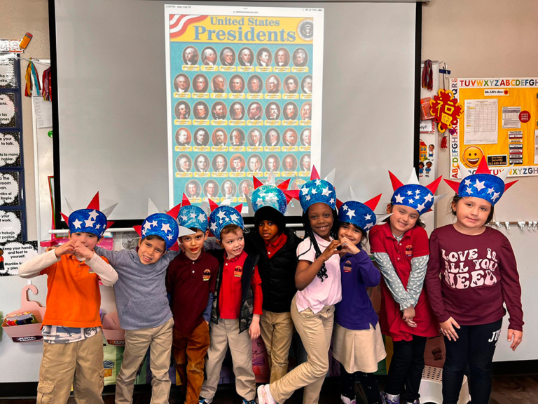 Children wearing festive hats pose in front of a poster of U.S. Presidents, smiling and celebrating together.