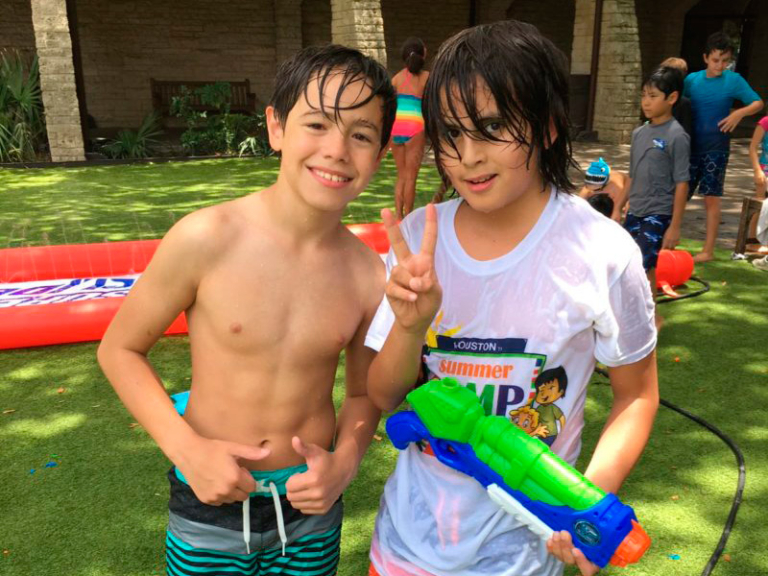 Two kids, wet from play, pose with a water gun, smiling and enjoying a fun summer day at camp.