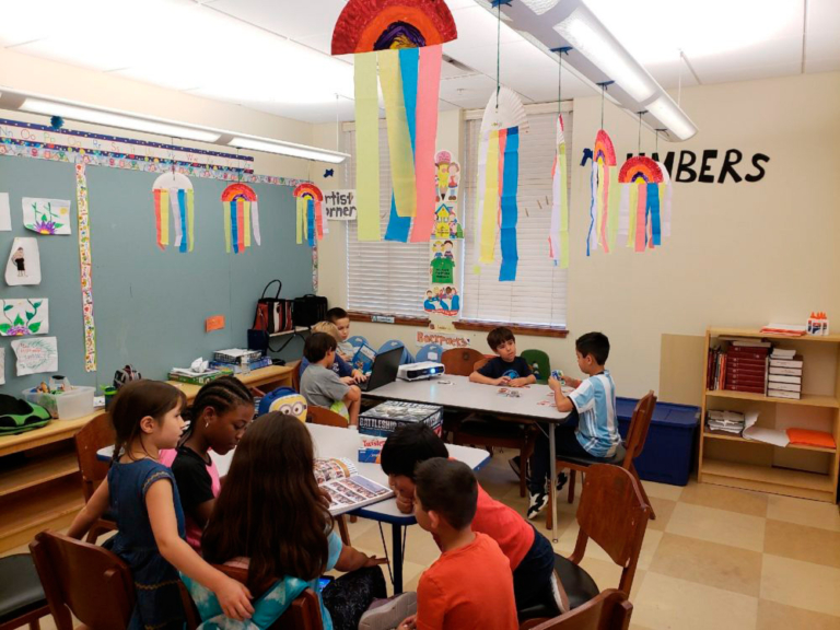 Kids work together in a colorful classroom filled with decorations, engaged in fun activities around the tables.