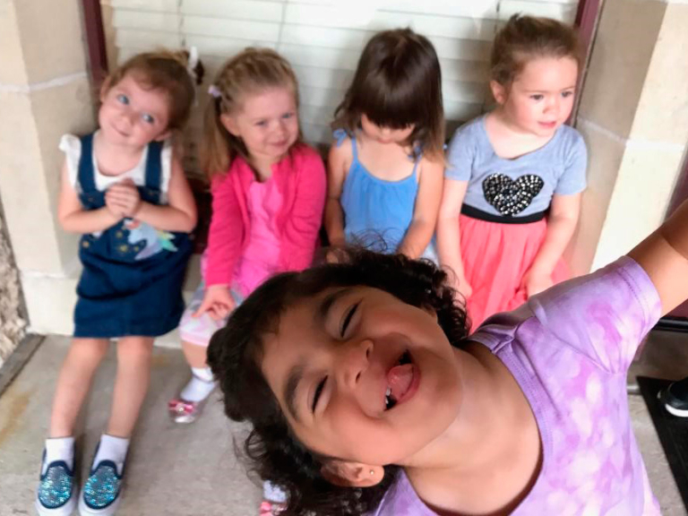 A girl playfully poses in front of her friends, who sit behind her, smiling and enjoying their time together.